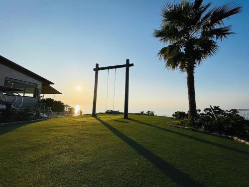 a palm tree and a swing in a field with the sunset at VILLA BLUEOCEAN AWAJIYA SOUTHヴィラブルーオーシャン淡路屋south in Awaji
