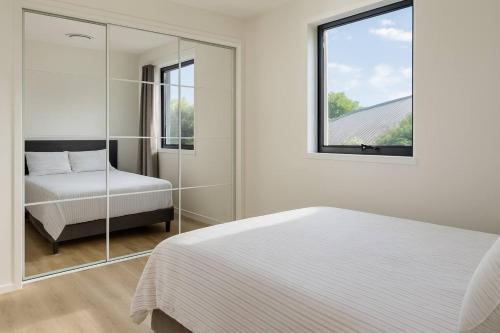 a white bedroom with a bed and a mirror at New & Stylish Veg 2-Bedroom Guest Retreat Near Brisbane Airport in Brisbane