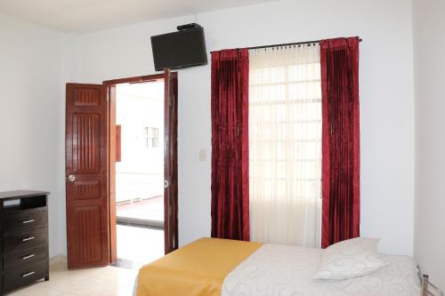 a bedroom with a bed with red curtains and a television at Hotel Abadia in Sogamoso