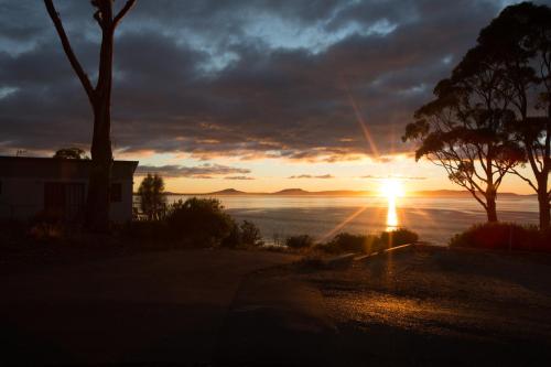 a sunset over the ocean with a house and trees at Swansea Beach Chalets in Swansea