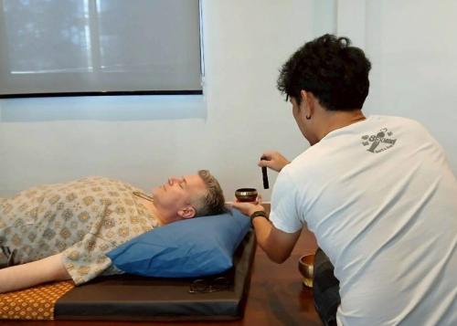 Bang ChakLittle Tree Hut的一个男人躺在床上，另一个男人正在给他递饮料