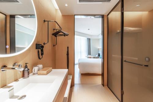 a bathroom with a sink and a mirror and a bed at JI Hotel Shanghai Pudong Airport Zhuqiao in Nanhui