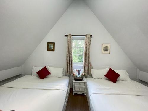 two beds in a attic room with a window at Chermonné House เฌอมอญ 