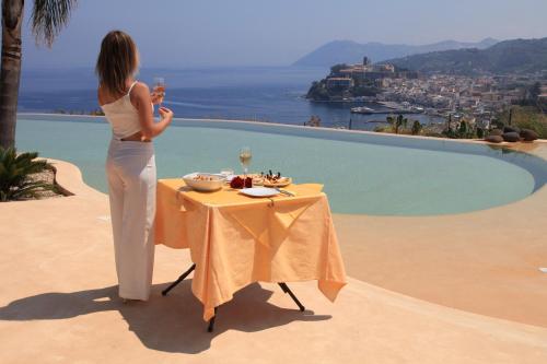 a woman standing next to a table with a glass of wine at Hotel Villa Enrica - Aeolian Charme in Lipari