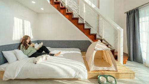 a woman sitting on a bed reading a book with a dog at Gapyeong Daengdaengi Dog Pension Silver in Gapyeong