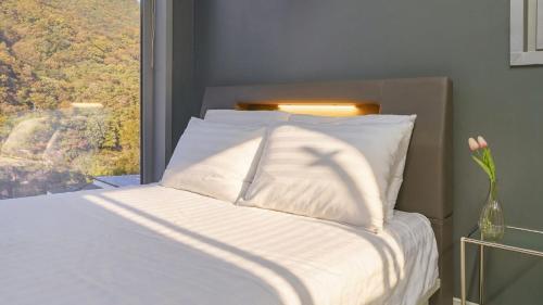 a bed with white sheets and a window with a vase with flowers at Hongcheon inmylife dokche pension in Hongcheon