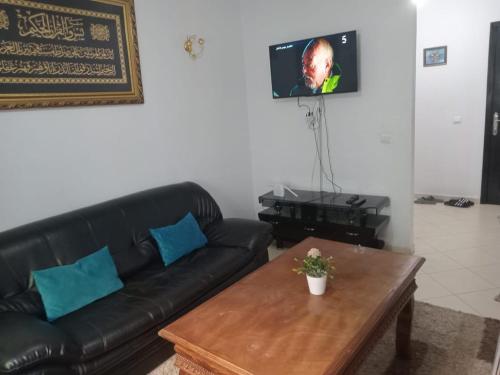 a living room with a black leather couch and a coffee table at Appartement Familial Proche Aeroport Bab Andalous Tanger in Tangier