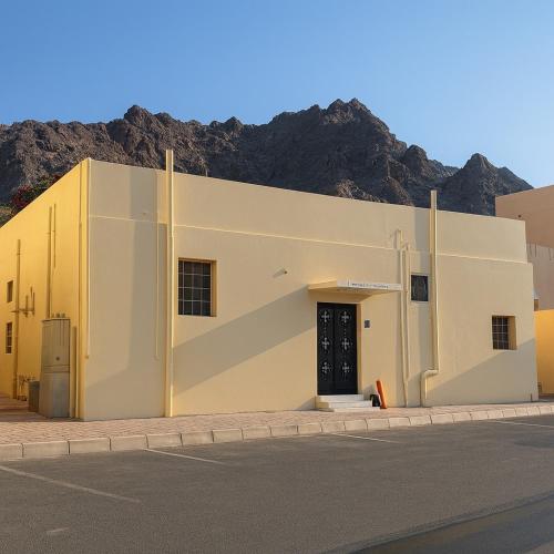 a large white building with a mountain in the background at Sikka Hostel in Muscat