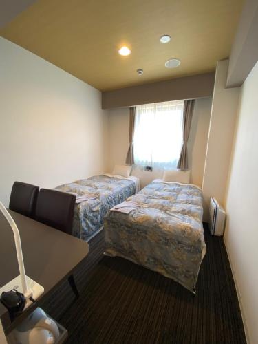a room with two beds and a desk and a window at Murayama Nishiguchi Hotel in Murayama