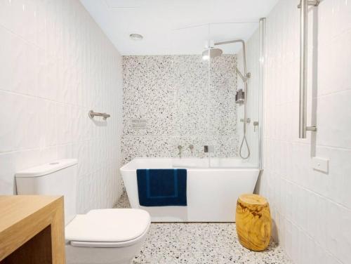 a white bathroom with a tub and a toilet at Corrigans Poolside Apartment Batehaven in Batehaven