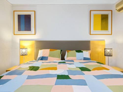 a bedroom with a colorful bed with two lamps at Corrigans Poolside Apartment Batehaven in Batehaven