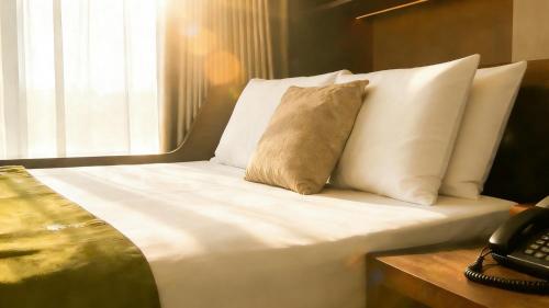 Una cama con sábanas blancas y almohadas junto a un teléfono. en The Purple Horse Hotel Beijing, en Beijing