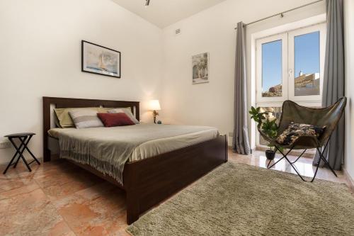 a bedroom with a bed and a chair and a window at Cherry Penthouse in Spinola Bay in St. Julianʼs