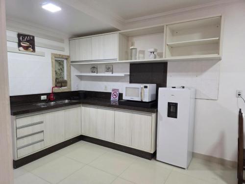 a kitchen with white cabinets and a white refrigerator at Flat Rota do Sol Bombinhas Centro 100 metros da praia - sem cozinha in Bombinhas