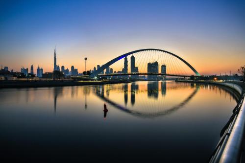 a bridge over a river with a city in the background at Luxury 1 Bedroom Canalfront Apartment with Burj Khalifa Views from Resort-Style Pool - Walk to Jumeirah Beach in Dubai