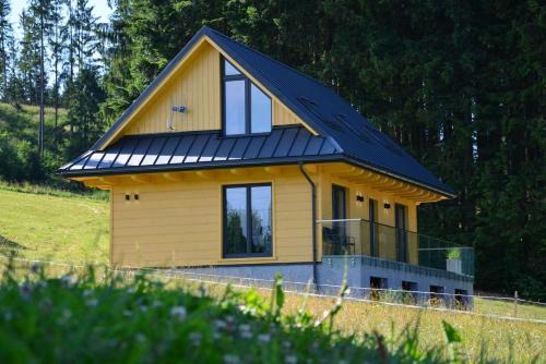 a small yellow house with a black roof at Anielskie chaty - domki z widokiem na góry in Sablówka