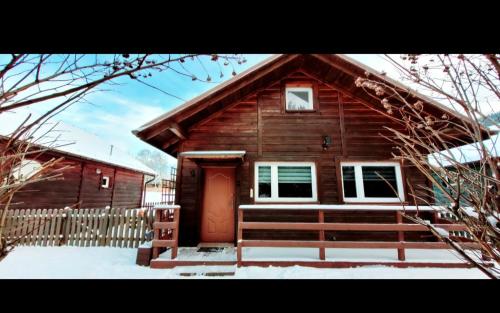 a wooden cabin with a red door in the snow at Stanica pod Zadzierną Domki całoroczne in Lubawka