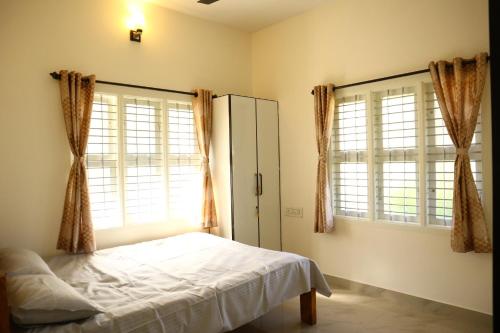 a bedroom with a bed and two large windows at Raghavendra Homestay in Kalyānpur