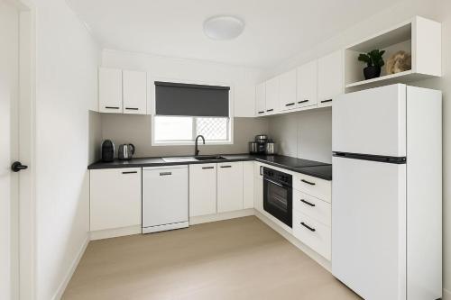 a white kitchen with white cabinets and a refrigerator at 2-Bedroom Charm near Mater Hospital Pimlico Townsville in Aitkenvale