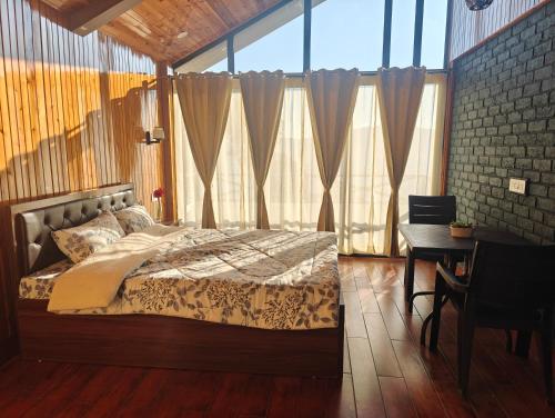 een slaapkamer met een bed, een bureau en ramen bij Meraki Cottage in Darjeeling