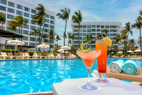 two cocktails on a table next to a swimming pool at Ocean Breeze Nuevo Vallarta in Nuevo Vallarta