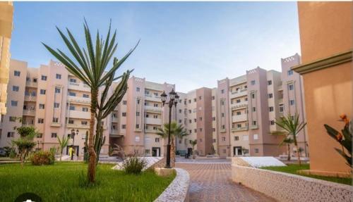 a large apartment building with palm trees in a courtyard at Chez Rime Cosy apartment with pool view in Mohammedia
