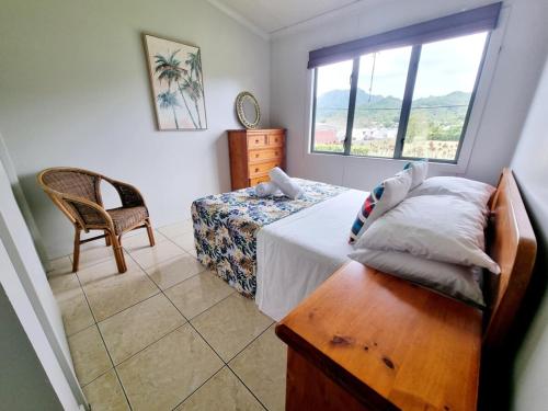 een slaapkamer met een bed, een stoel en een raam bij Natura Nikao Beachside 3BM Villa in Avarua