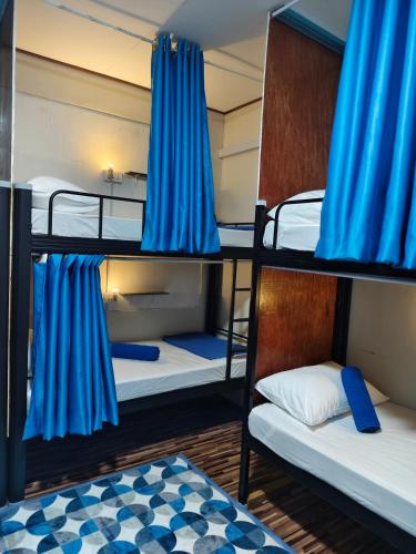 a room with three bunk beds with blue curtains at Anchor Point Hostel and Cafe in Pulau Langkawi