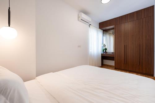Schlafzimmer mit einem weißen Bett und einem Holzschrank in der Unterkunft Quince Apartments in Podgorica