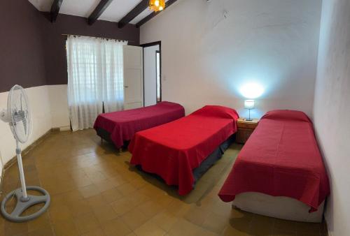 a room with two beds with red sheets and a fan at Casa zona CUCÚ de 2 dormitorios in Villa Carlos Paz