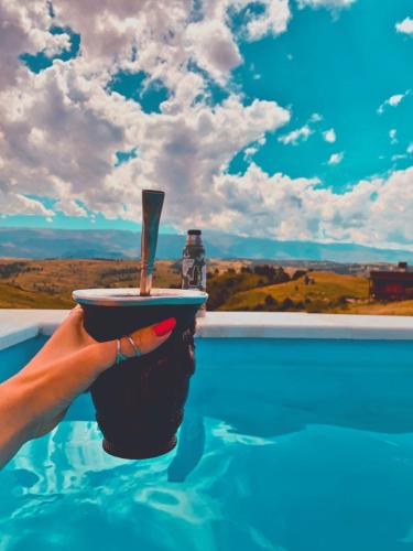 a hand holding a cup with a drink on top of a pool at La Autóctona in Villa Yacanto