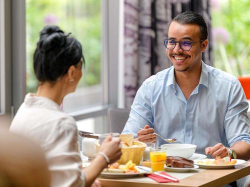 Um homem e uma mulher sentados à mesa comendo. em Mercure Hotel Stuttgart Airport Messe em Estugarda