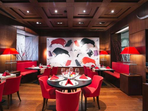 a restaurant with red chairs and tables and a large painting at Pullman Bucharest World Trade Center in Bucharest