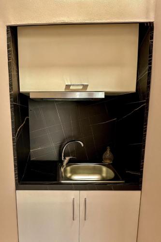 a kitchen with a sink and a black tiled wall at Midtown Cozy Apartment in Tirana