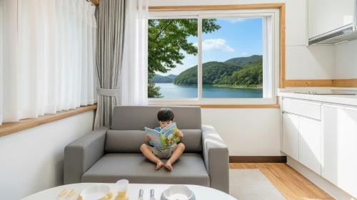 Ein Kind sitzt auf einem Stuhl und liest ein Buch vor einem Fenster. in der Unterkunft Chuncheon El Dorado Kid's Pension in Gapyeong