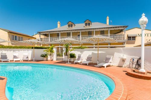 a pool with chairs and umbrellas in front of a house at The Clifton Motel in Bunbury