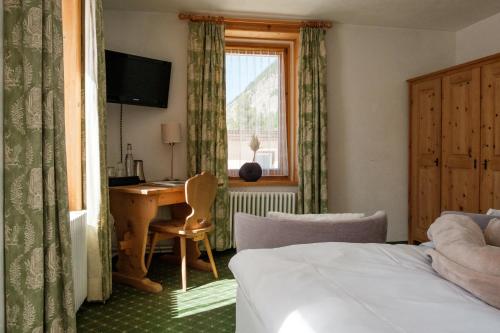 Un dormitorio con una cama y un escritorio y una ventana. en Hotel Bernina, en Pontresina