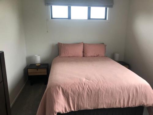 Schlafzimmer mit einem Bett mit rosa Bettwäsche und einem Fenster in der Unterkunft Country Cottage Centrally Located in Tauwhare