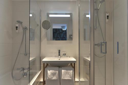 a white bathroom with a sink and a shower at Mercure Paris Saint Cloud Hippodrome in Saint-Cloud
