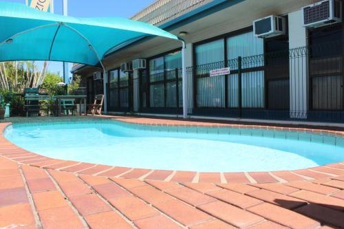 
a pool with a blue umbrella in front of a building at Fitzroy Motor Inn in Rockhampton
