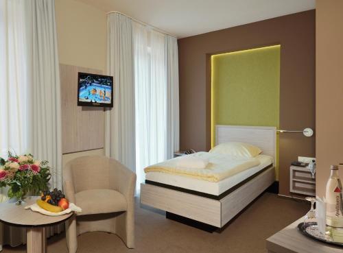 a bedroom with a bed and a chair and a tv at Akzent Hotel Haus Surendorff in Bramsche