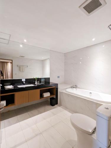 a bathroom with a tub and a toilet and a sink at Astanaraya Suites Hotel in Jakarta