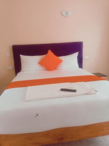 een bed met een oranje kussen en een afstandsbediening erop bij Wonderful Guesthouse in Kimana