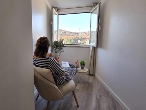 a woman sitting in a chair looking out a window at Aconchego da Vila in Castelo de Vide