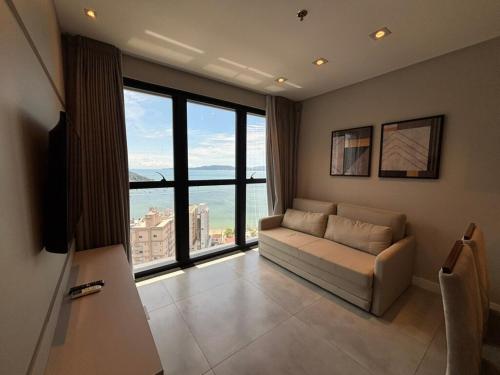 een woonkamer met een bank en een groot raam bij Vista Mar - Suíte, Cozinha Completa, Até 4 pessoas in Itapema
