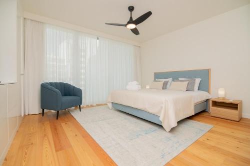 a white bedroom with a bed and a blue chair at Bayline X in Armação de Pêra