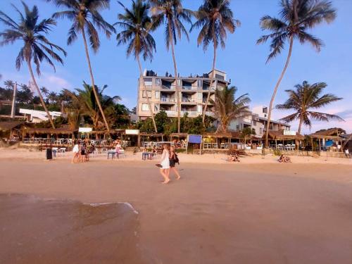 Dos mujeres caminando por la playa con un hotel al fondo en Suncoast Beach Hotel, en Mirissa