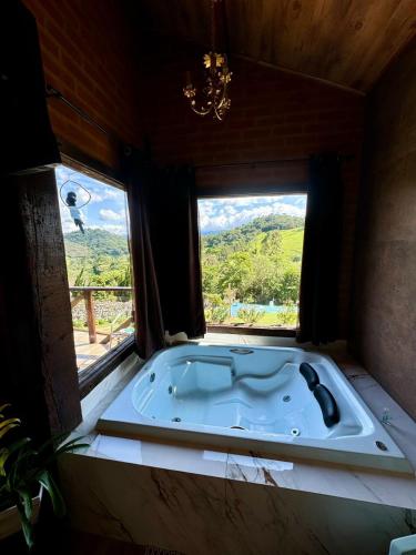 a bath tub in a room with a window at Chale Da Terra Brasil, Piscina, Hidro dupla, cozinha, lareira, vista espetacular in Santo Antônio do Pinhal