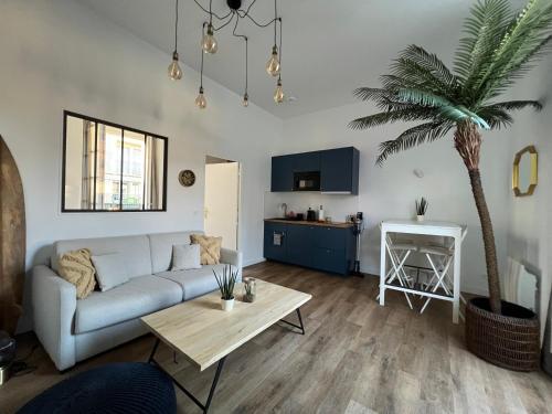 a living room with a couch and a palm tree at Le Laurencin Sens - La Plage - Cœur de ville in Sens