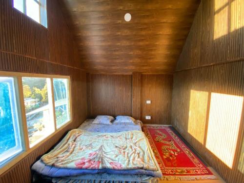 a small bed in a wooden room with two windows at Maitreya Homestay in Tawang